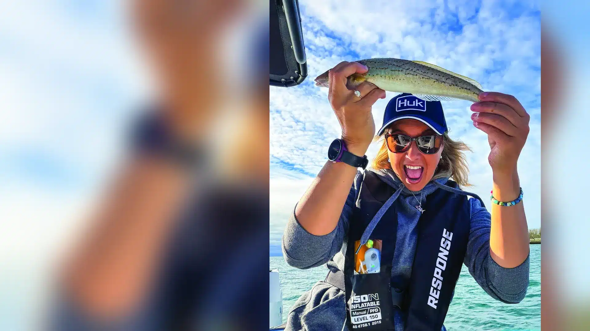 Woman wearing a RESPONSE 150N inflatable life jacket holding up a fish on a boat